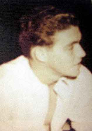 A young man is captured in profile, exhibiting light brown hair and a contemplative expression, dressed in a white shirt.